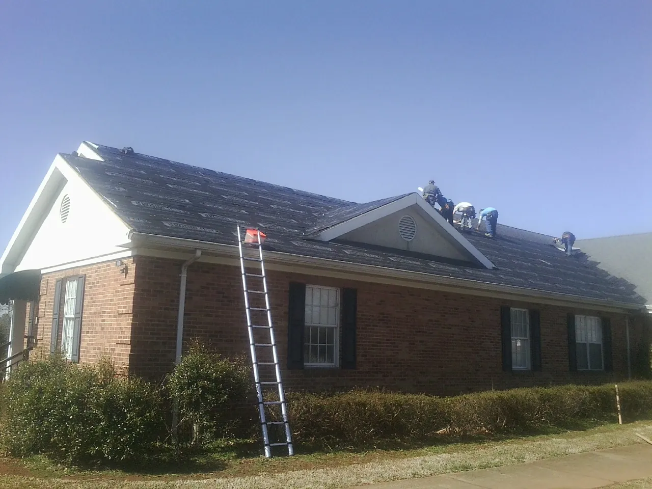 Crew tearing shingles off a brick ranch roof with a ladder set — Emergency Roof Repair work by our crew in Loudon
