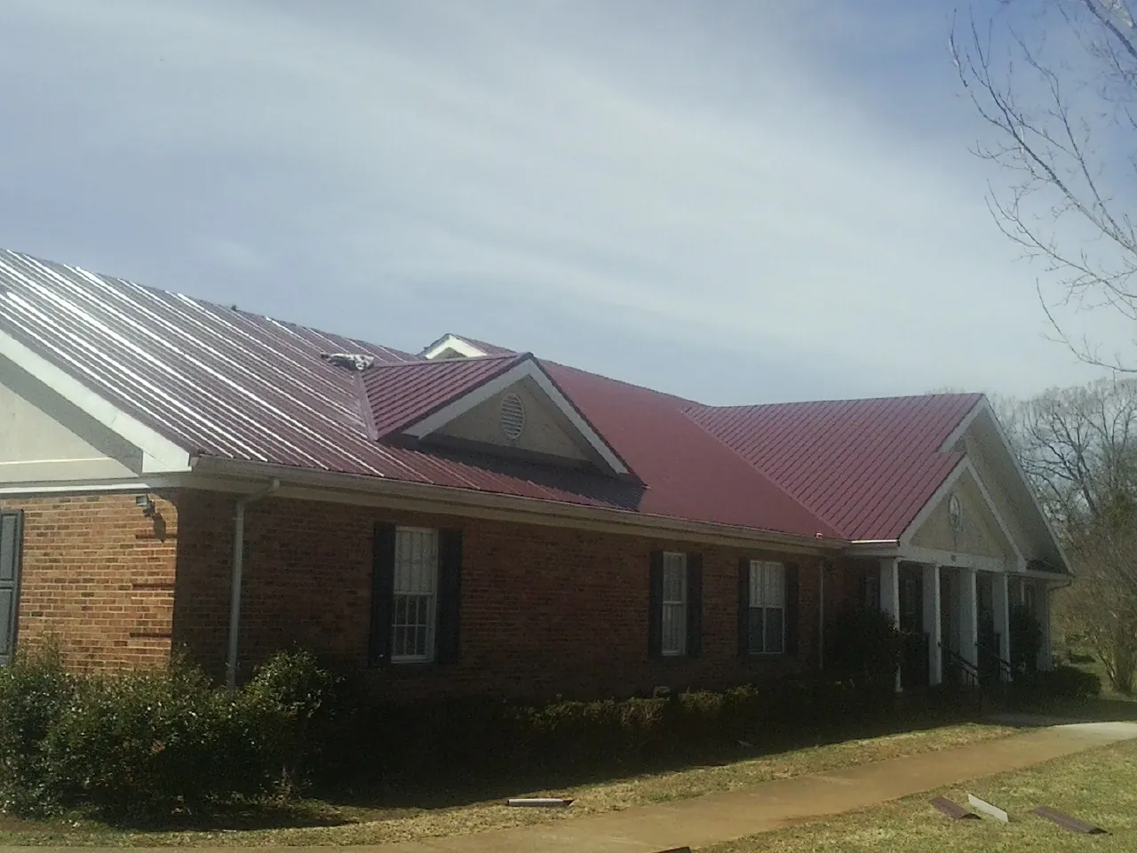 Red metal roof with gabled entries on a long brick building, from a Hail Damage Roof Repair job in Loudon