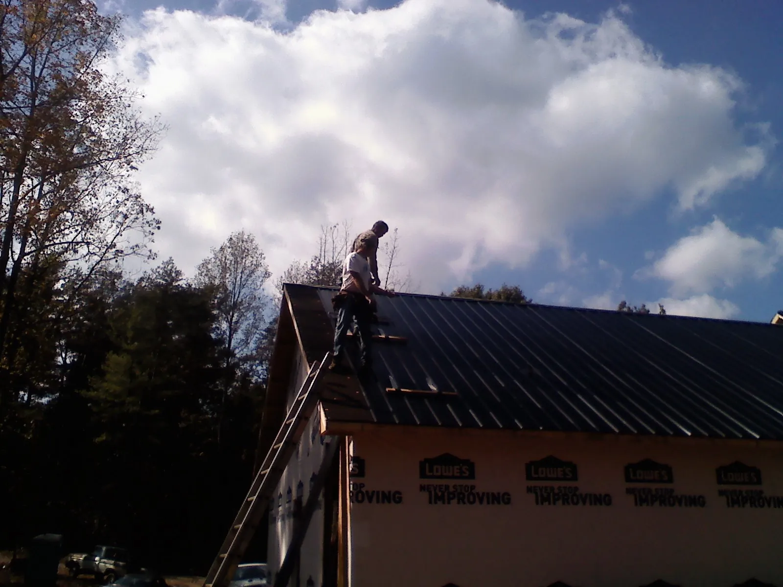 Roofer fastening dark metal panels high against a cloudy sky, from a Roof Inspection job in Loudon